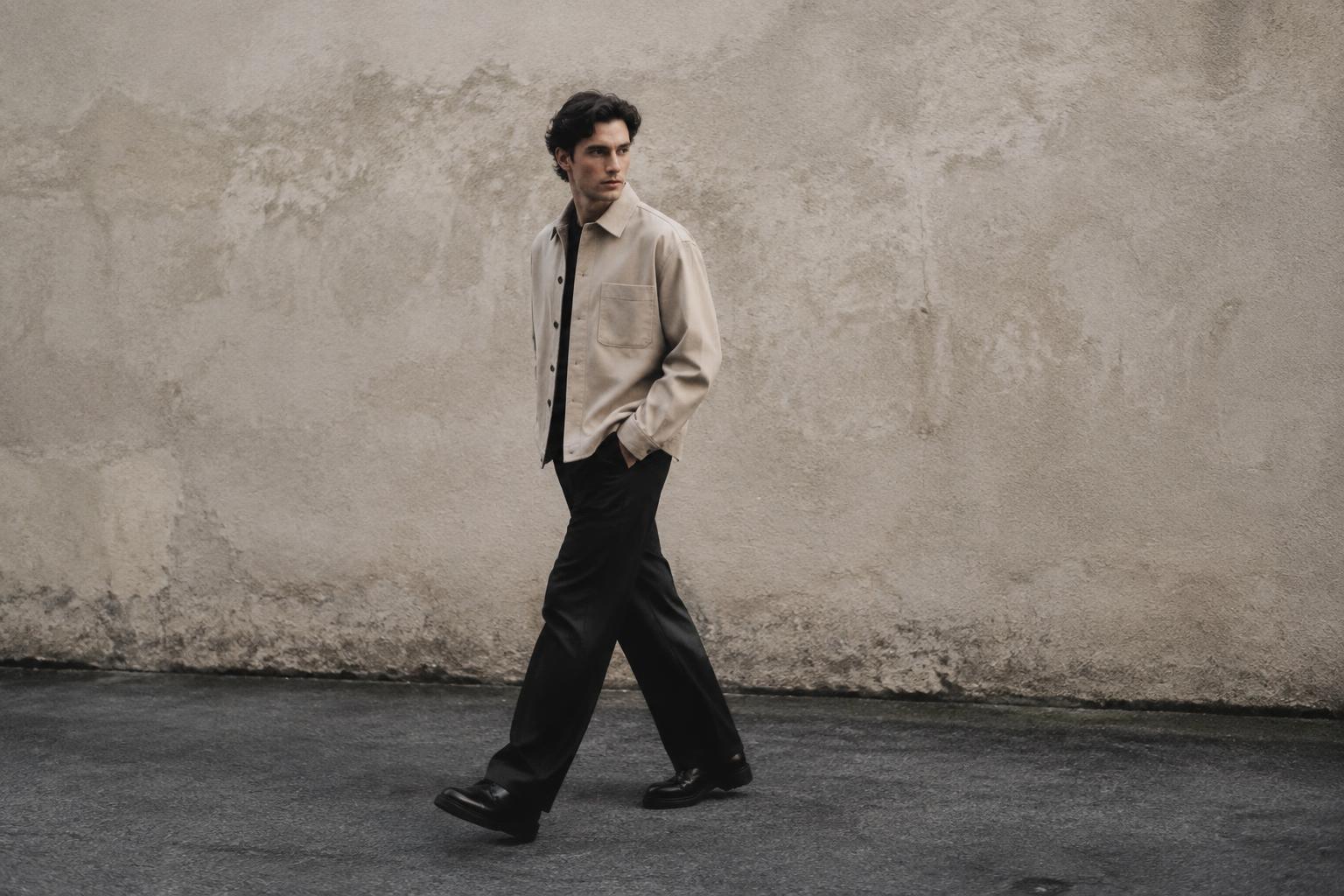 Model in a stone overshirt walking past a plaster wall